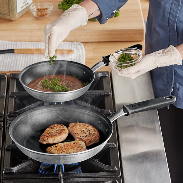 A woman cooking meat in a Vollrath Wear-Ever frying pan.