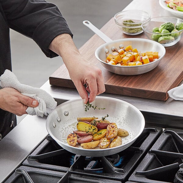 A person cooking potatoes in a Vollrath Arkadia frying pan.