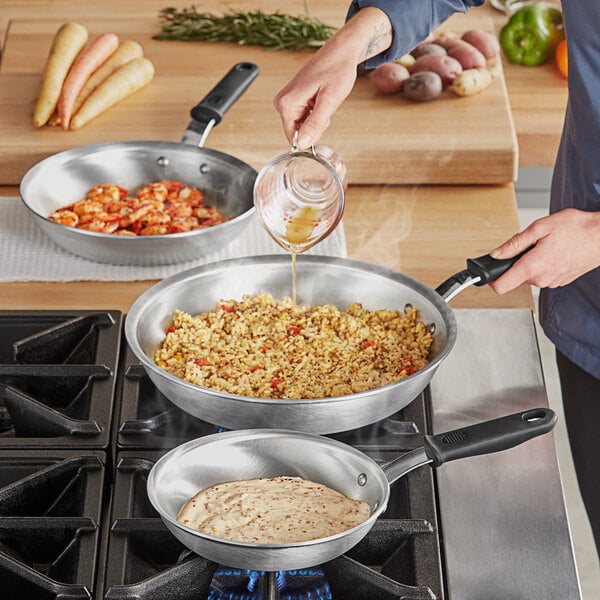 A person pouring liquid into a Vollrath Wear-Ever frying pan on a stove.