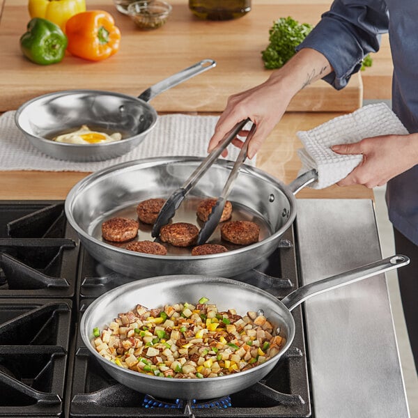 A woman cooking food in a Vollrath frying pan on a stove.