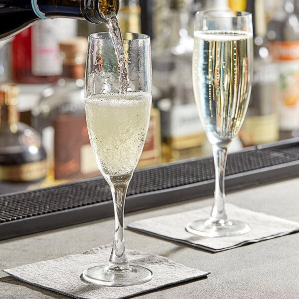 A person pouring champagne into a glass on a table in a cocktail bar.