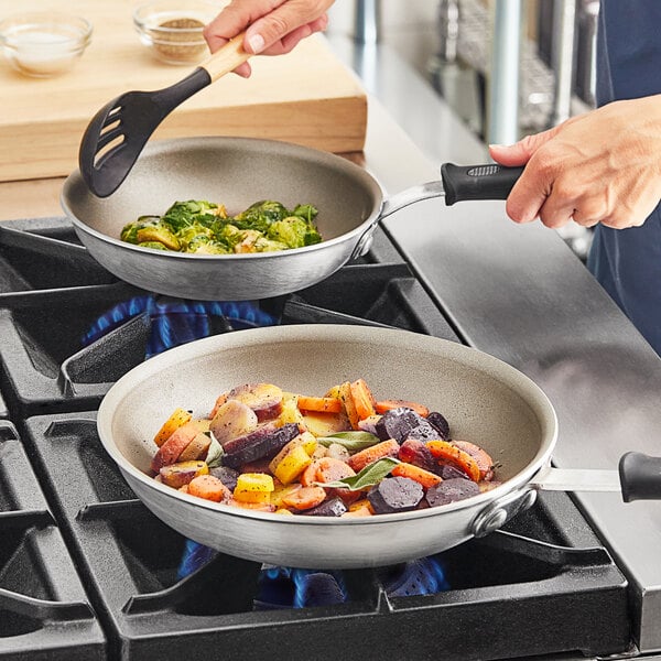 A hand stirring vegetables in a Vollrath Wear-Ever non-stick fry pan on a stove.