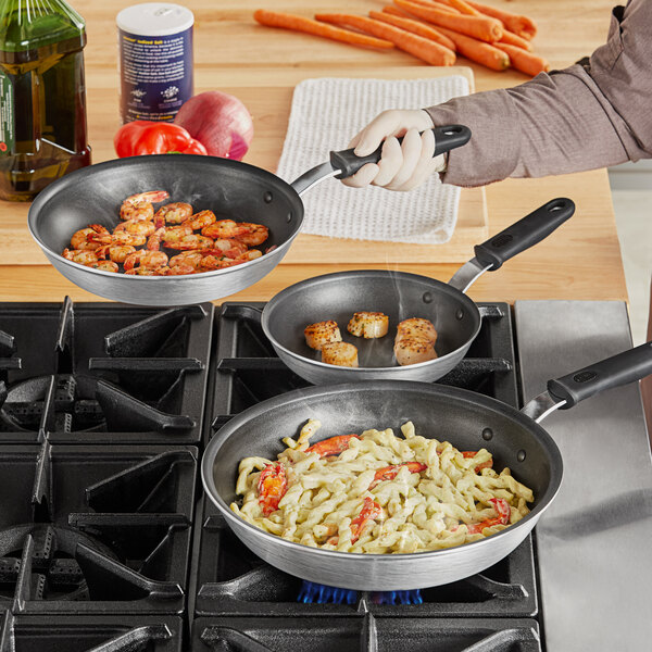 A person cooking food in a Vollrath Wear-Ever non-stick frying pan.