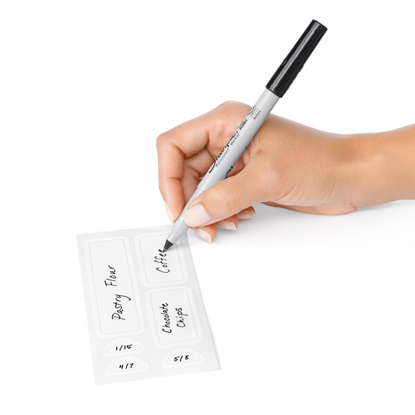 A hand holding a pen writing on an OXO Good Grips POP Removable label