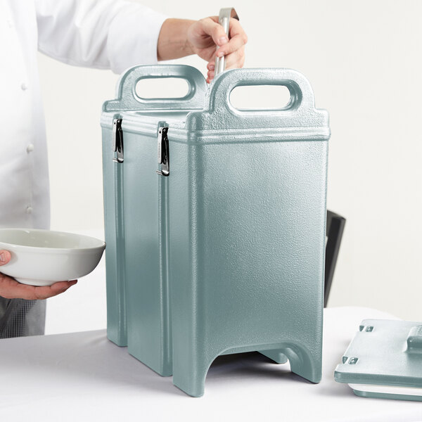A person holding a white bowl and a Cambro insulated soup carrier.