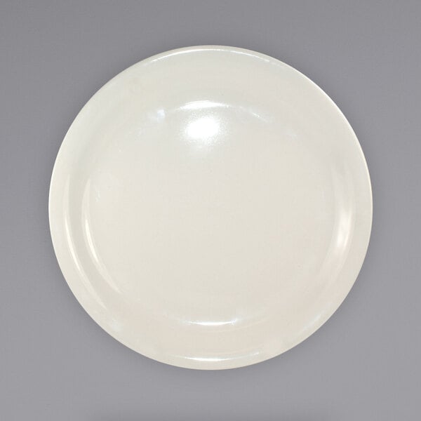 A close up of an International Tableware Valencia ivory stoneware plate with a narrow rim on a white surface.