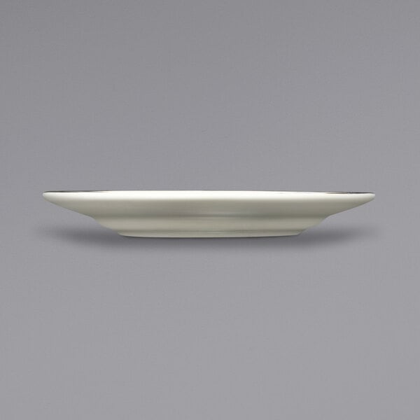 An International Tableware ivory stoneware plate with a gold rim on a white surface.
