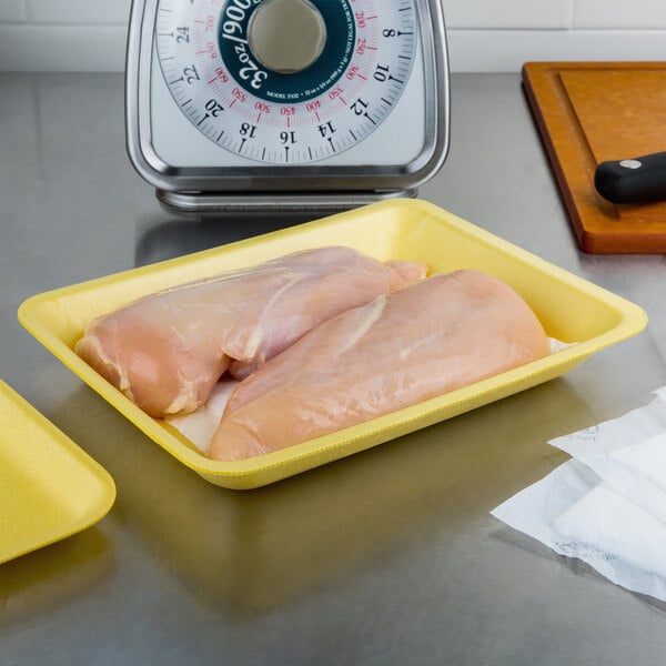 Two raw chicken breasts on a yellow CKF foam meat tray on a counter.