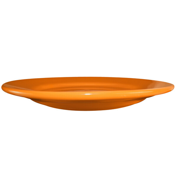 An orange International Tableware stoneware plate with a rolled edge and wide rim.