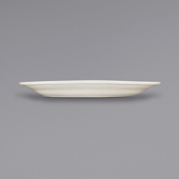 An International Tableware Roma ivory stoneware platter with a wide rim on a white surface with a black border.
