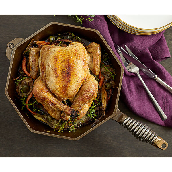 A FINEX octagonal cast iron skillet with chicken and vegetables on a table.