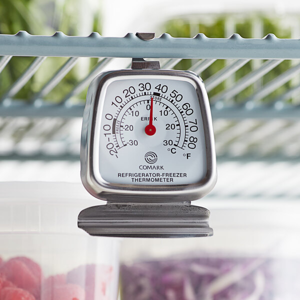A Comark refrigerator/freezer thermometer hanging from a shelf.