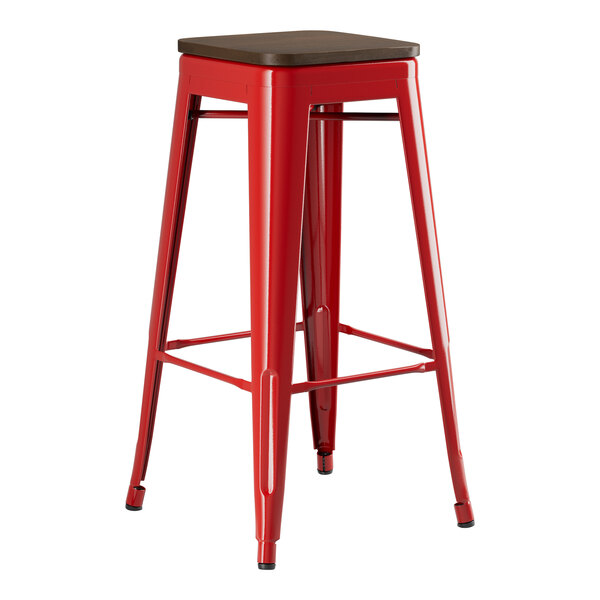 A red Lancaster Table & Seating backless barstool with a walnut wood seat.