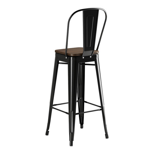 A black metal Lancaster Table & Seating barstool with a walnut wood seat.