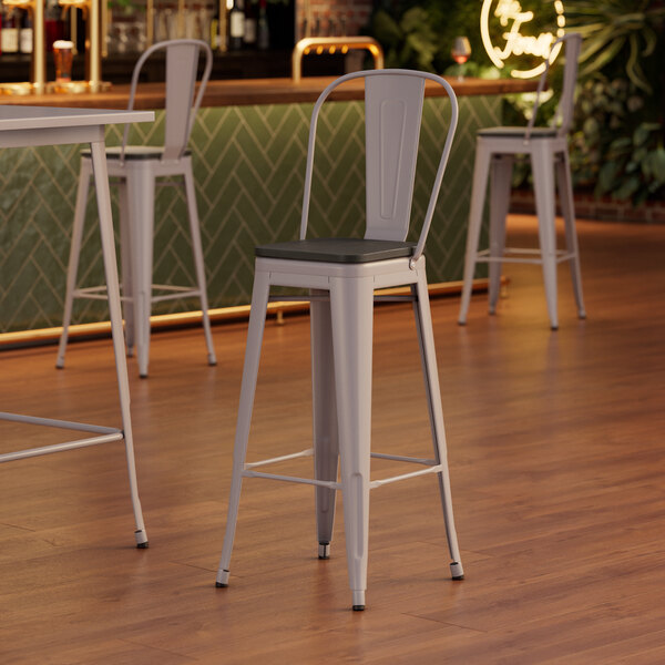 Lancaster Table & Seating Alloy Series Nickel Gray Indoor Cafe Barstool with Black Wood Seat at a table in a restaurant.