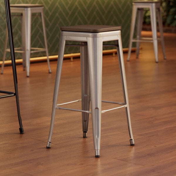 Three Lancaster Table & Seating metal backless barstools with walnut wood seats.