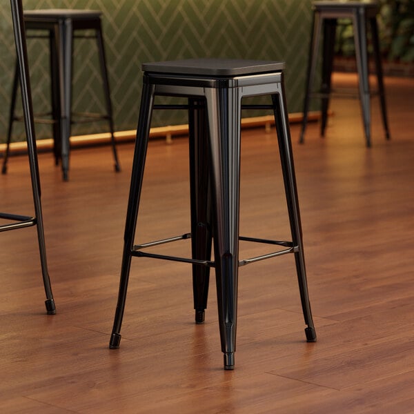 A close-up of a Lancaster Table & Seating black metal bar stool with a black wood seat.