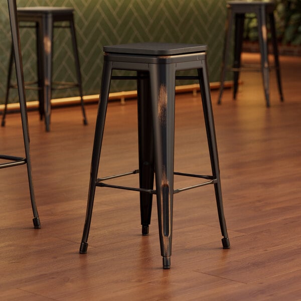 Three Lancaster Table & Seating black metal barstools with black wood seats on a wood floor.