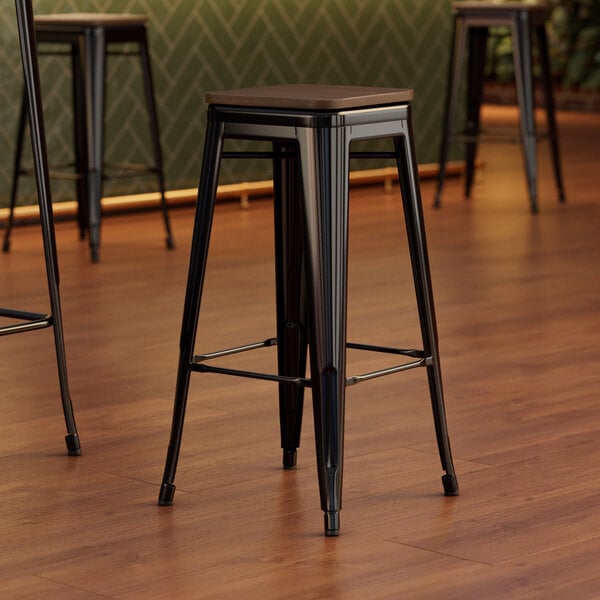 Three Lancaster Table & Seating black metal barstools with walnut seats.