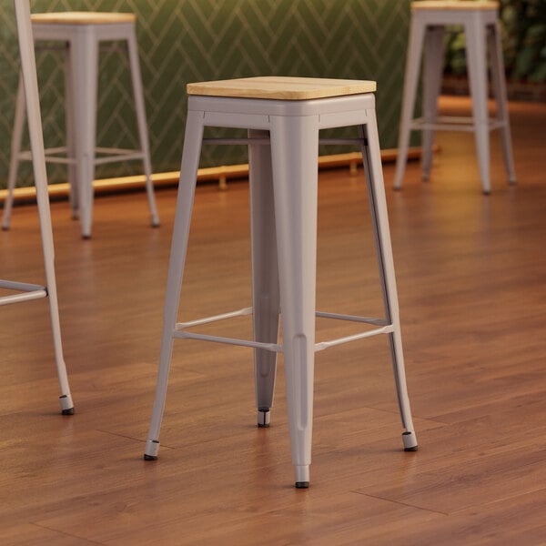Three Lancaster Table & Seating nickel gray metal bar stools with natural wood seats.