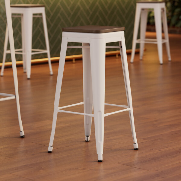 Three Lancaster Table & Seating pearl white metal barstools with walnut seats.