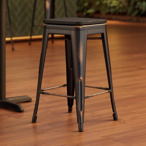 A Lancaster Table & Seating distressed copper stool with a black wood seat on a wood floor.