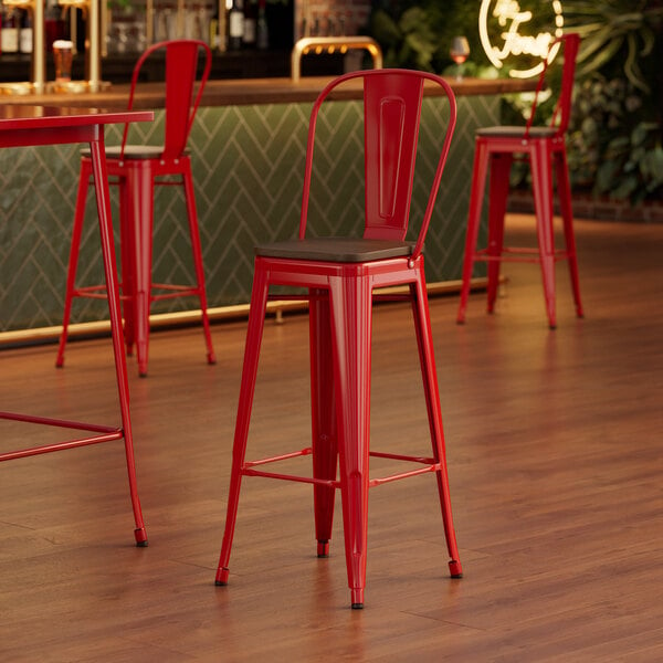 A red Lancaster Table & Seating barstool with a walnut seat.