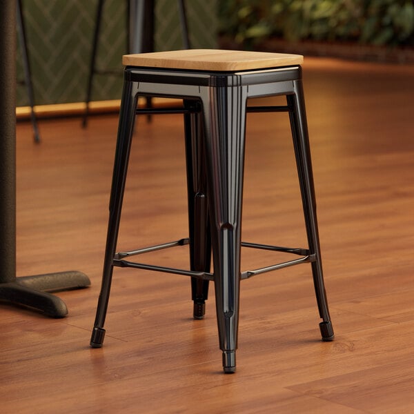 A Lancaster Table & Seating black backless counter height stool with a natural wood seat on a wood floor.