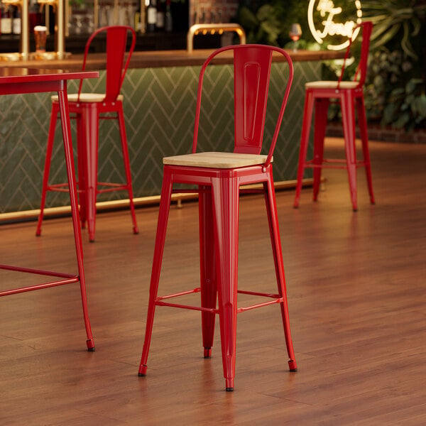 A Lancaster Table & Seating red metal barstool with a natural wood seat.