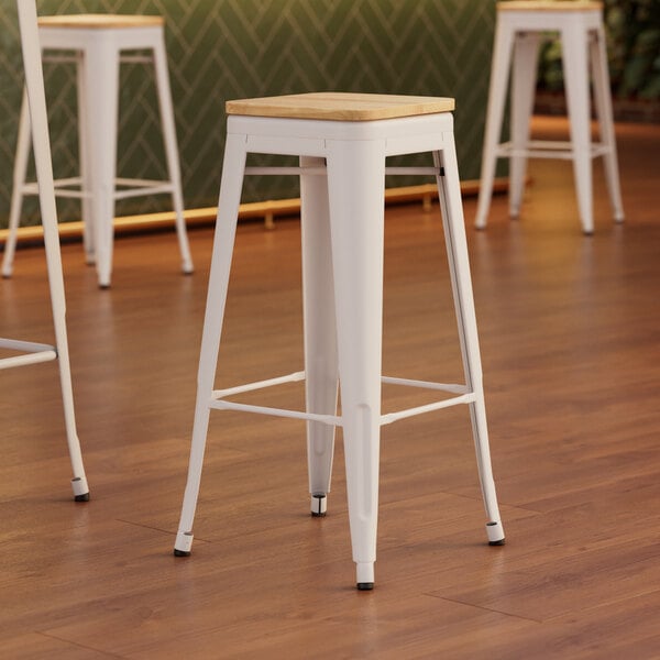 Three Lancaster Table & Seating white metal bar stools with natural wood seats.