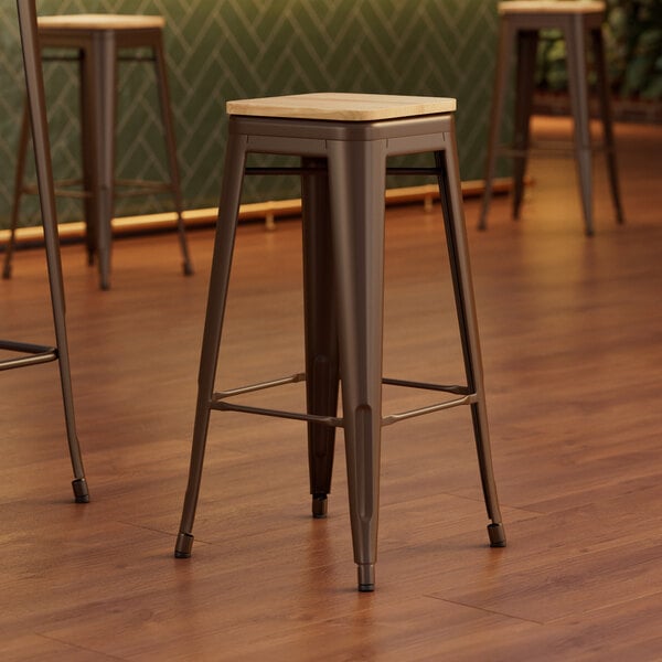 Three Lancaster Table & Seating copper backless barstools with natural wood seats.