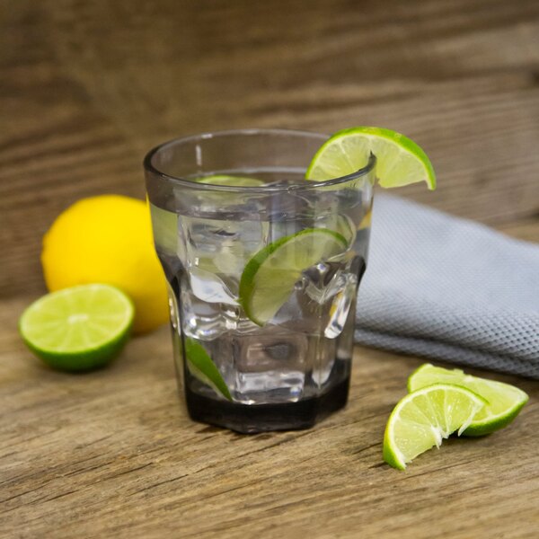 A Carlisle smoke plastic tumbler of water with ice and lime slices on a table.