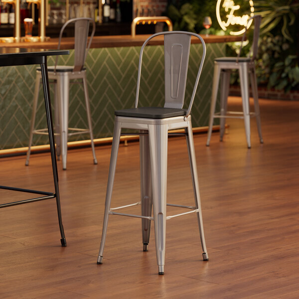 A Lancaster Table & Seating silver barstool with a black wood seat.