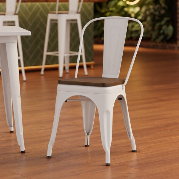 A white Lancaster Table & Seating metal chair with a walnut wood seat on a white table.