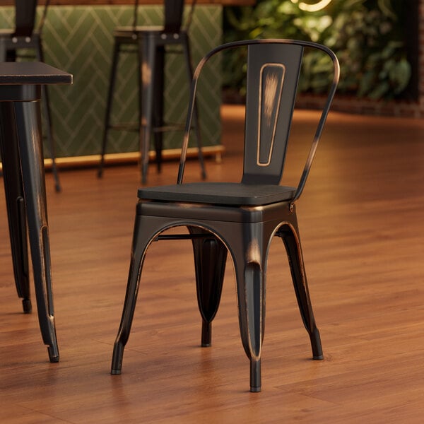 A Lancaster Table & Seating distressed copper metal chair with a black wood seat at a wooden table in a restaurant.