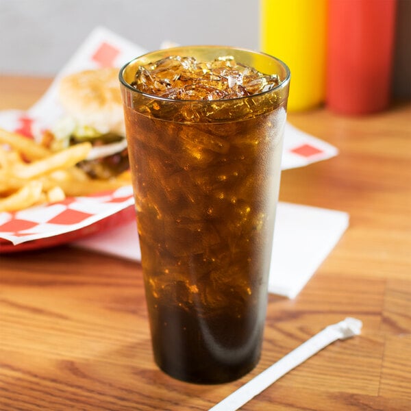 A Carlisle amber plastic tumbler with soda and ice on a table with a burger.