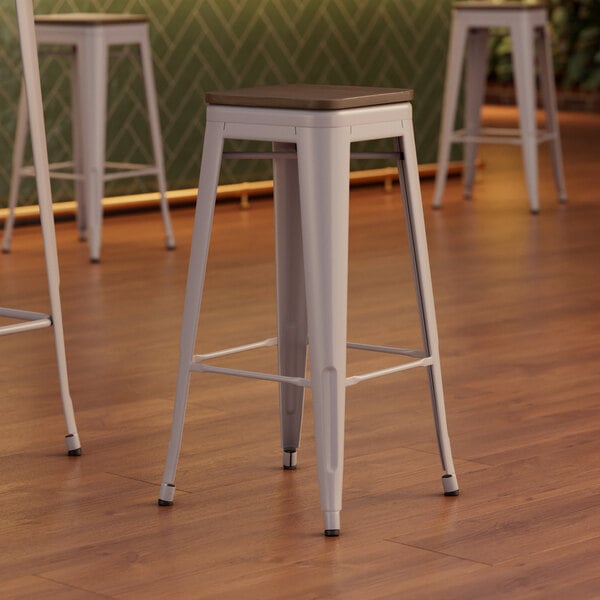 Three Lancaster Table & Seating nickel gray metal barstools with walnut wood seats.