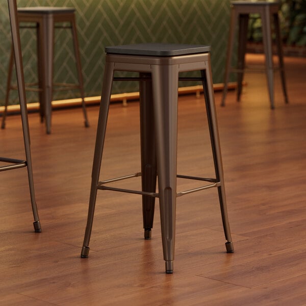 A close-up of a Lancaster Table & Seating backless copper bar stool with a black wood seat.