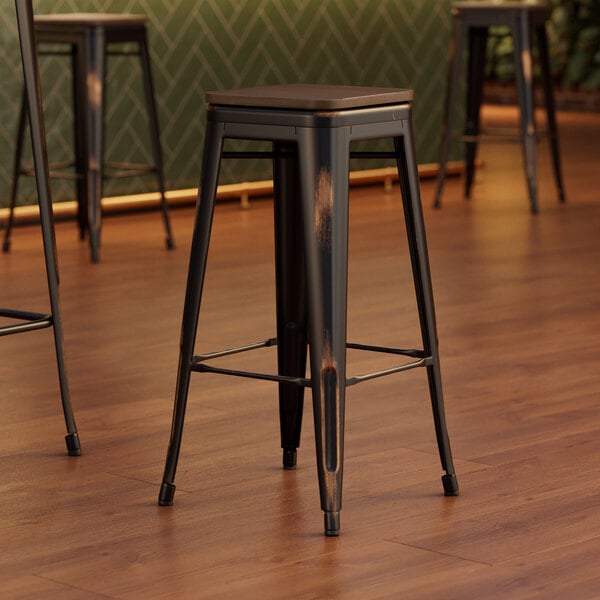 Three Lancaster Table & Seating distressed copper metal barstools with walnut wood seats at a table in a coffee shop.