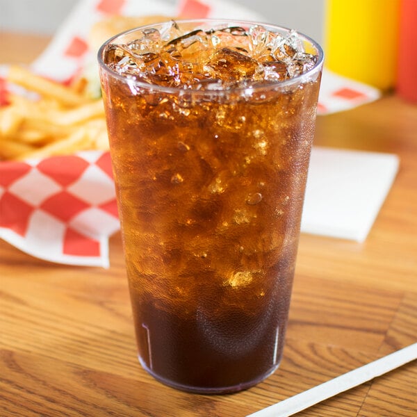 A Carlisle clear plastic tumbler with brown liquid, ice, and a straw on a table.