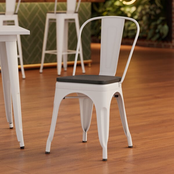 A white Lancaster Table & Seating metal chair with a black wood seat.