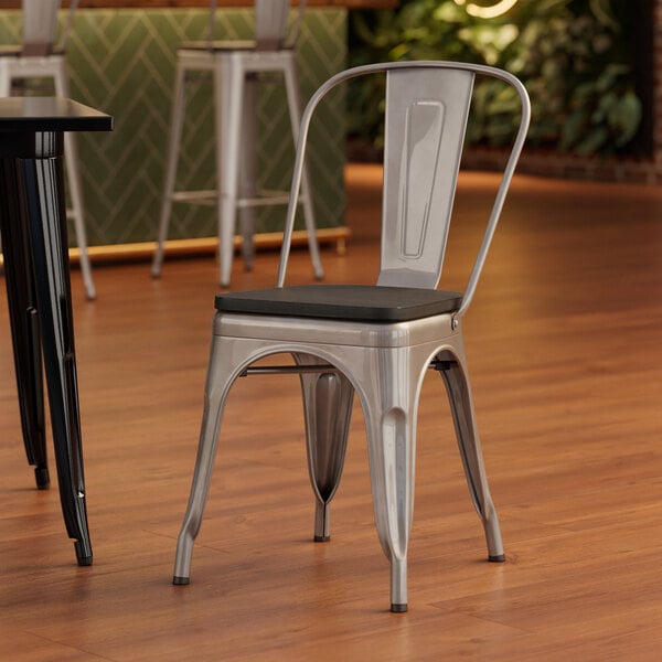A Lancaster Table & Seating metal cafe chair with a black wood seat sits at a table.