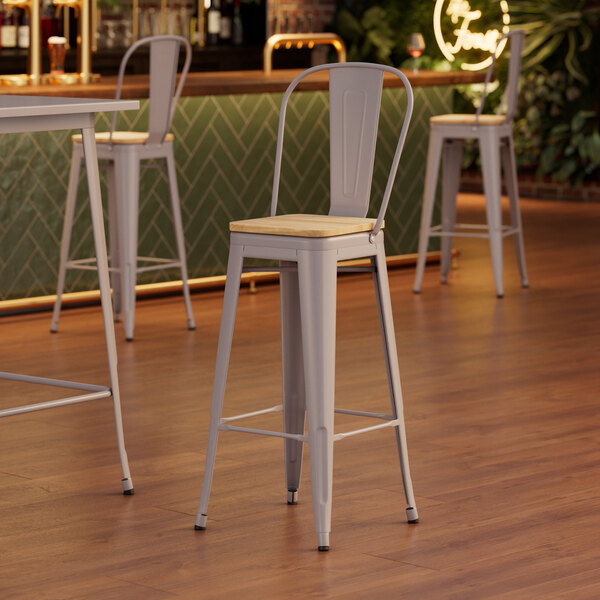 Lancaster Table & Seating Alloy Series Nickel Gray Indoor Cafe Barstool with Natural Wood Seat at a restaurant table.