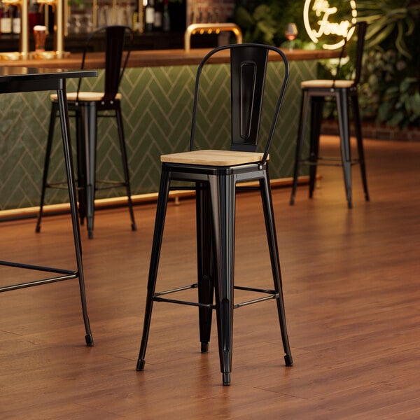 A Lancaster Table & Seating black metal cafe barstool with a natural wood seat.