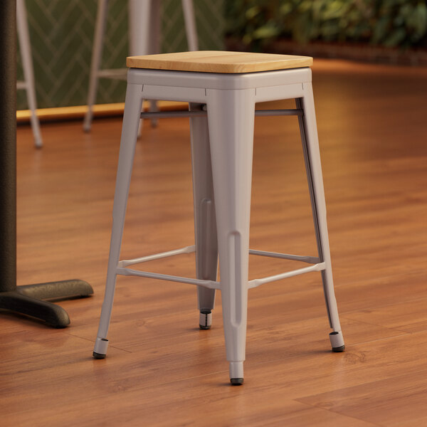 A Lancaster Table & Seating gray metal stool with a natural wood seat on a wood floor.