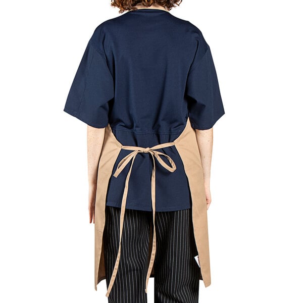 A woman wearing a khaki Uncommon Chef apron with brown trim.