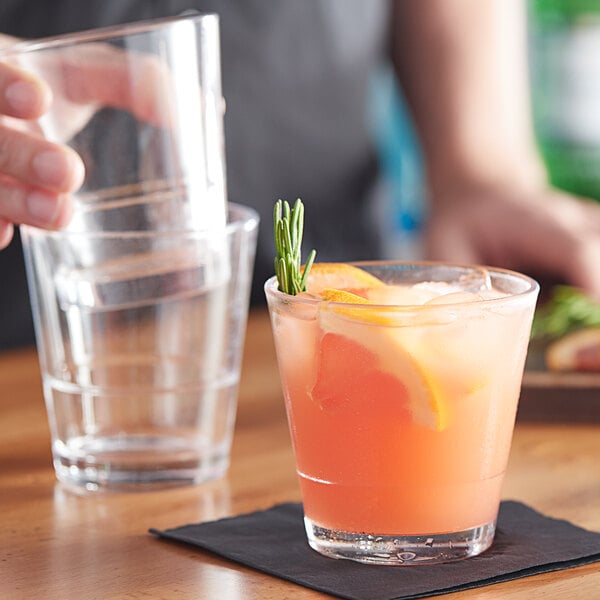 A person pouring a drink into an Acopa Select stackable rocks glass with a slice of orange on the rim.