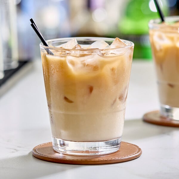 A clear 12 oz. stackable rocks glass filled with an iced beverage, placed on a round coaster.