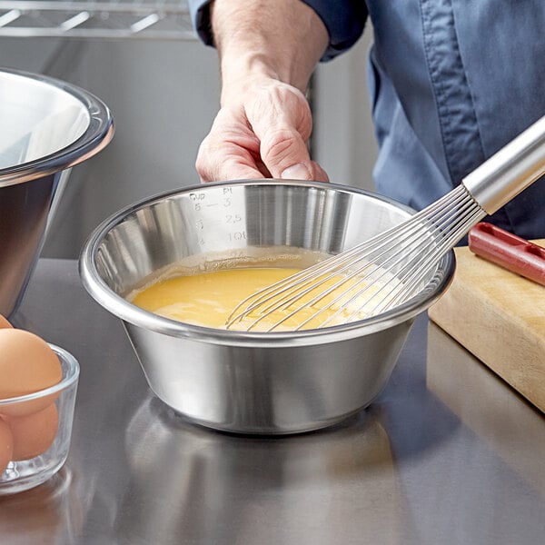 A person whisking eggs in a stainless steel mixing bowl.