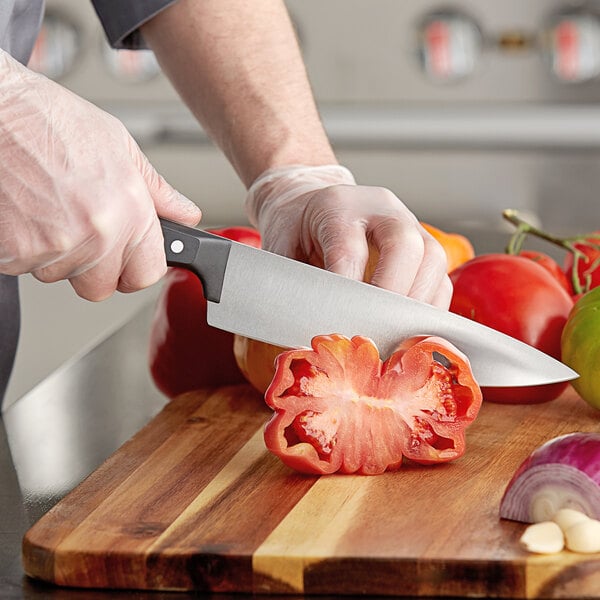 A person in gloves using a Wusthof Gourmet Cook's Knife to cut a tomato.